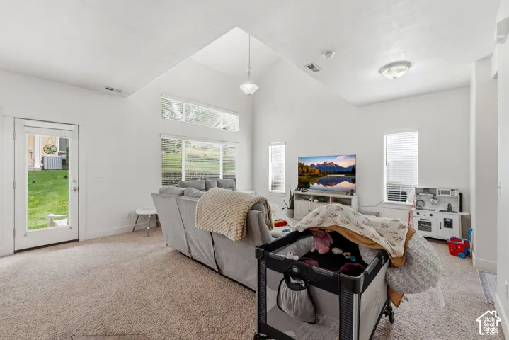 Vaulted ceiling with pendant lighting, multiple windows providing natural light, glass-paneled door, and neutral-toned carpeting