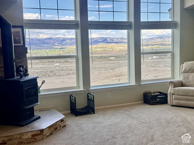Large windows with mountain scenery, a wood-burning stove with a stone and tile hearth, and carpeting