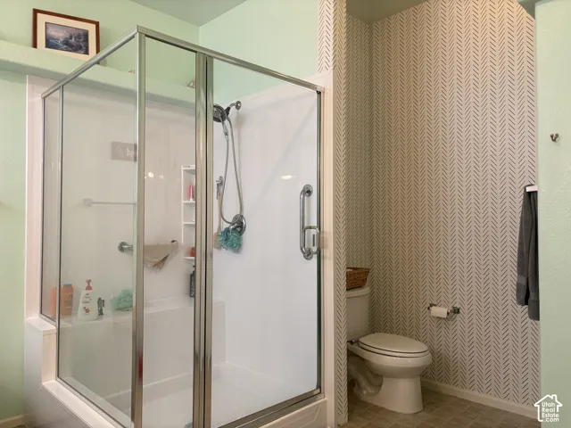 Enclosed shower with metallic frame, wall-mounted handheld shower fixture, built-in grab bars, and patterned wallpaper