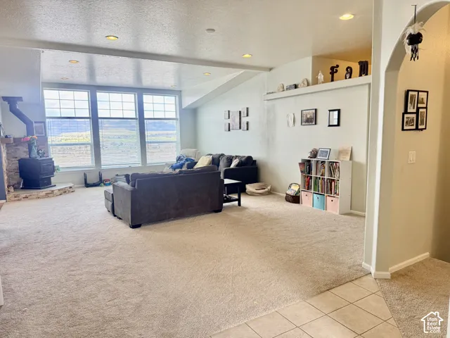 Spacious living area featuring large picture windows, recessed lighting, a stone-clad wood-burning stove, and neutral-toned carpeting
