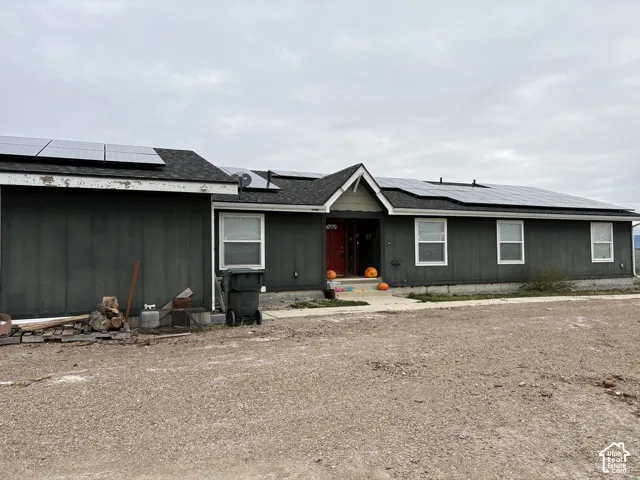 Single-story exterior featuring dark vertical siding, a pitched roof with integrated solar panels, and a red front entrance door