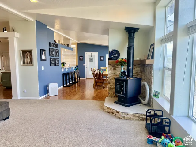 Wood-burning stove with stone surround, large windows, wood-finish flooring, and a breakfast bar with built-in shelving