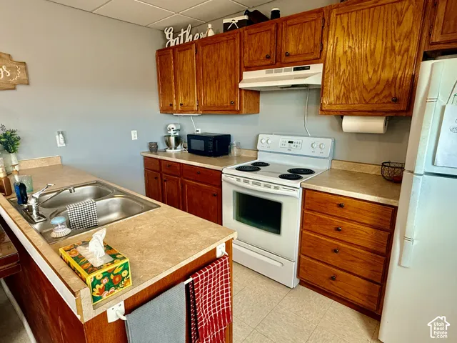 Kitchen featuring wood cabinetry, laminate countertops, a double basin stainless steel sink, and a white electric range with overhead ventilation
