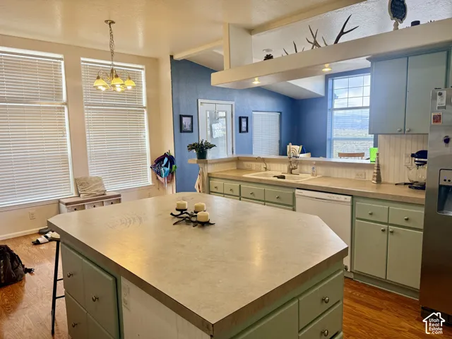 Kitchen featuring a central island, light-toned countertops, light green cabinetry, and wood-finish flooring