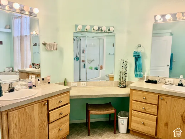 Dual vanity with integral sinks, neutral countertops, wood-finish cabinetry, and framed mirrors with overhead lighting