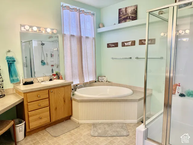 Built-in corner soaking tub, clear glass shower enclosure, vanity with integrated sink, wood-finish cabinetry, and overhead lighting