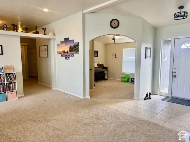 Entryway with tiled flooring, leading to a carpeted living space with recessed lighting and an arched doorway