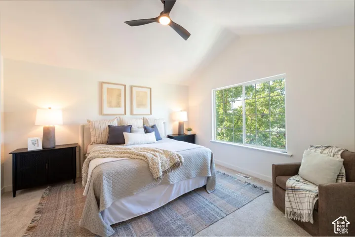 Vaulted ceiling with an integrated ceiling fan, expansive window, carpeted flooring, and two built-in nightstands