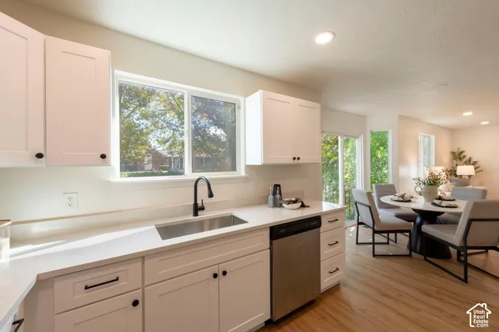 Kitchen featuring white shaker cabinetry, stainless steel dishwasher, undermount sink with a matte black faucet, light-toned countertops, and wood-finish flooring