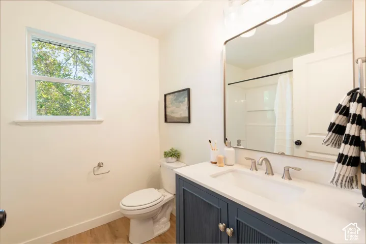 Wood-finish flooring, single-pane window, flush-mounted lighting, vanity with integrated basin, shower with white paneling