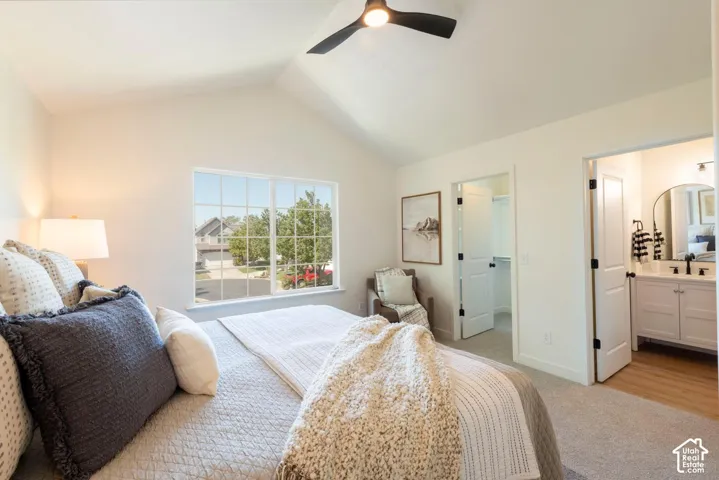 Vaulted ceiling, ceiling fan, large window with grid pattern, white vanity with black fixtures, and wood-finish flooring in the adjoining space