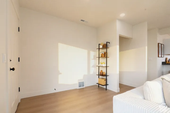 Light-toned wood-finish flooring, white painted walls, recessed ceiling lighting, and a built-in wall shelf