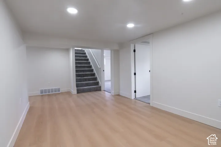 Light wood-finish flooring with white baseboards, recessed ceiling lighting, and freshly painted white walls