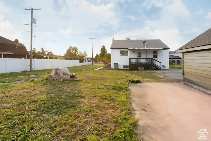 Expansive backyard featuring a white vinyl fence, gravel driveway, and a white exterior home with a dark-stained wood deck