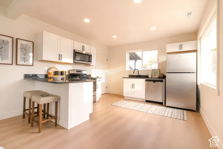 White shaker cabinetry, stainless steel appliances, dark stone countertops, wood-finish flooring, and recessed lighting