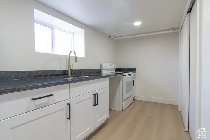 White shaker cabinetry with matte black hardware, dark stone-finish countertops, light wood-finish flooring, and a window above the sink