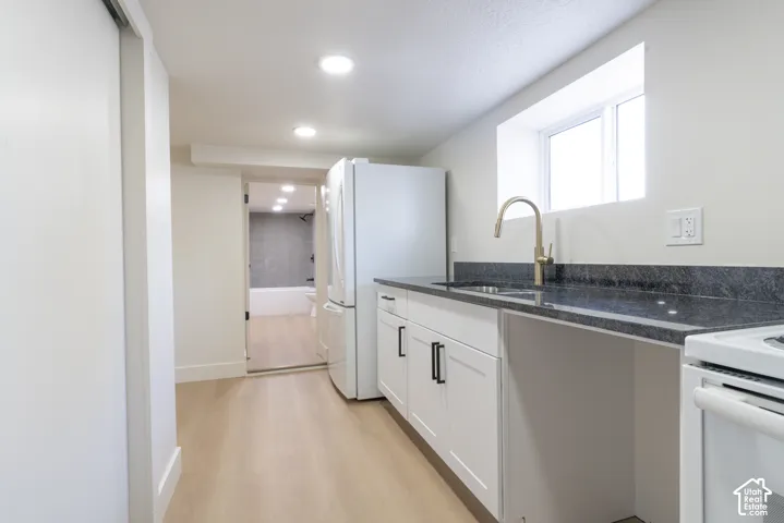 Kitchenette featuring a stainless steel sink with a high-arc faucet, dark speckled countertop, white cabinetry with black hardware, and light-tone wood-finish flooring