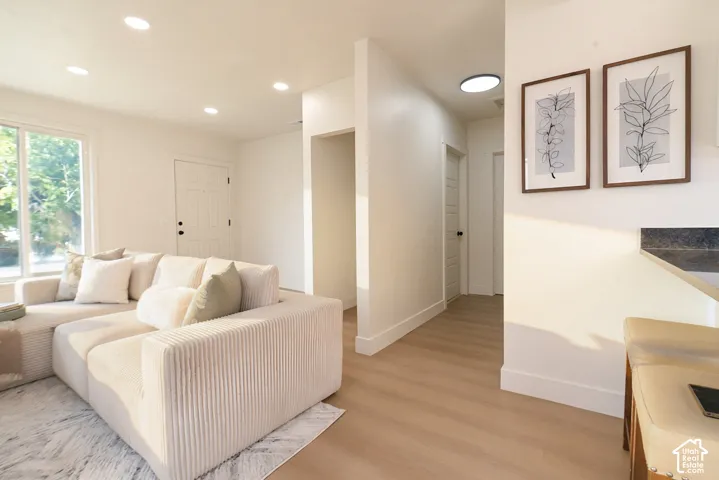Contemporary living space featuring a light-filled layout with recessed ceiling lighting, wood-finish flooring throughout, and a neutral color palette