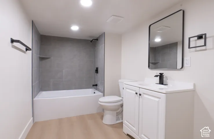Bathroom featuring a white vanity with integrated sink, black hardware throughout, recessed lighting, and a bathtub with gray tile surround