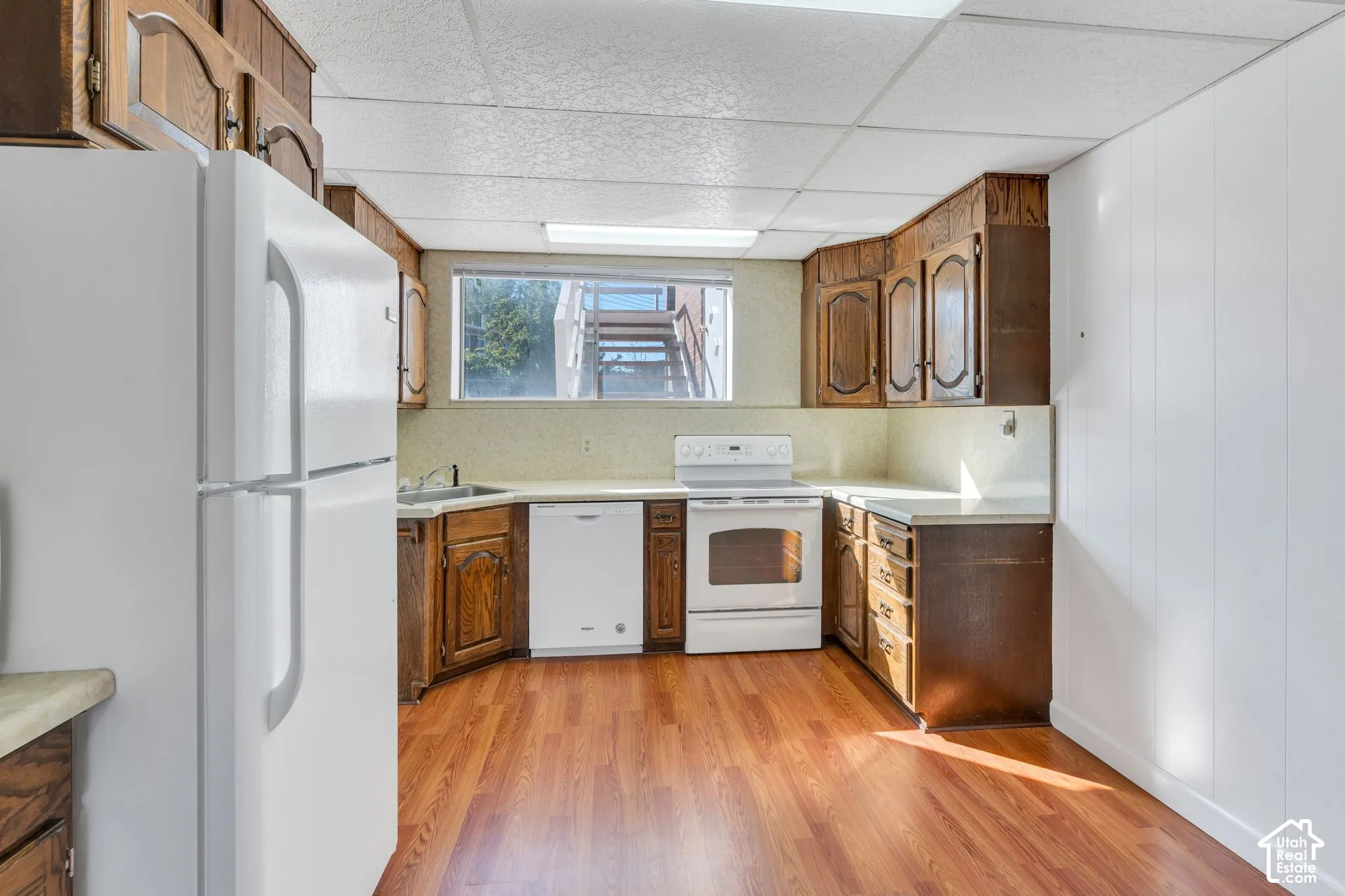 Kitchen featuring wood-finish flooring, white appliances, dark wood cabinetry, and a drop ceiling