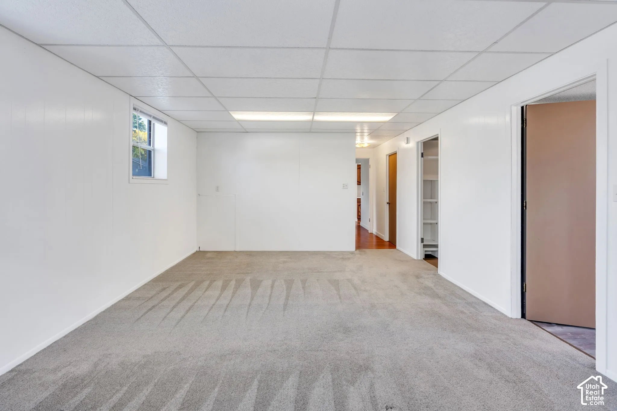 Carpeted flooring, drop ceiling, recessed lighting, white paneling, and a single window