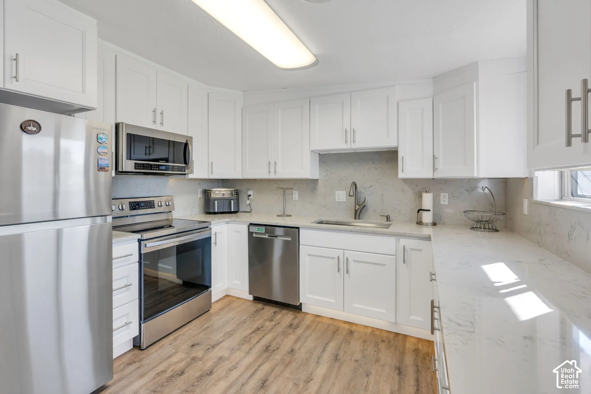 White cabinetry, wood-finish flooring, stainless steel appliances, white countertops, and a full-height backsplash