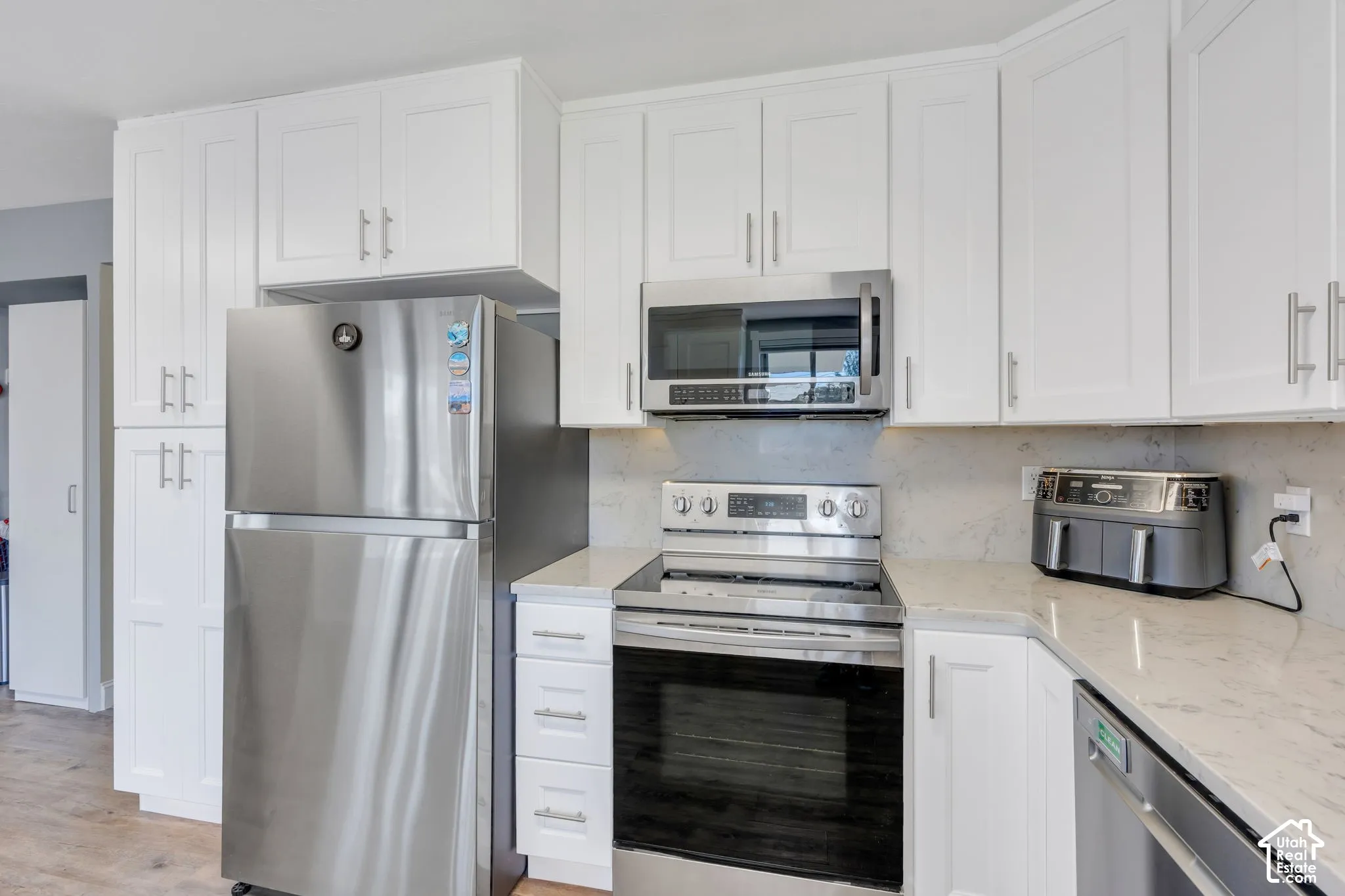 White shaker-style cabinetry, stainless steel appliances, light-toned countertops, and a coordinating backsplash