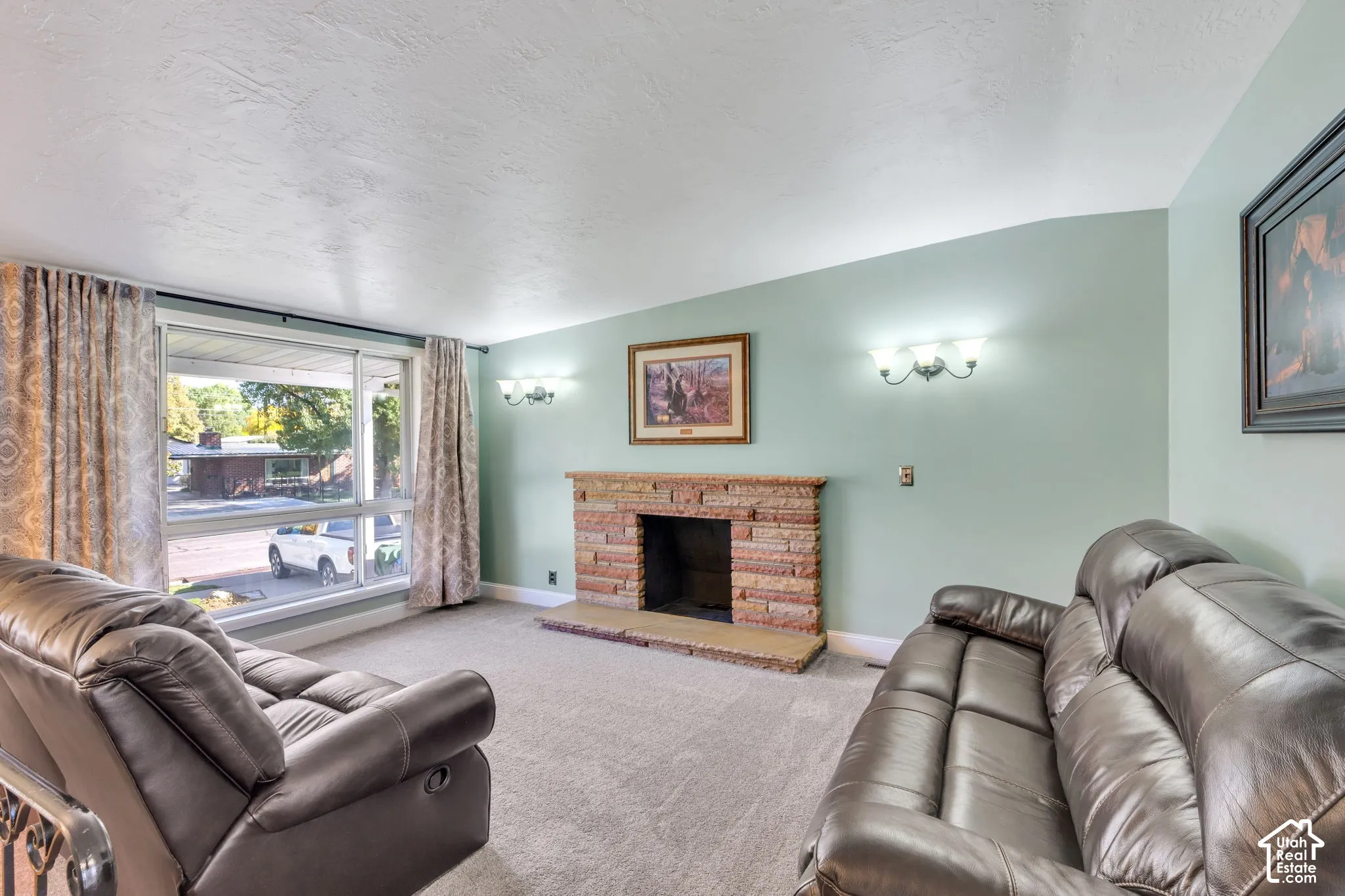Built-in fireplace with a stone surround and hearth, large picture window, and wall-mounted light fixtures