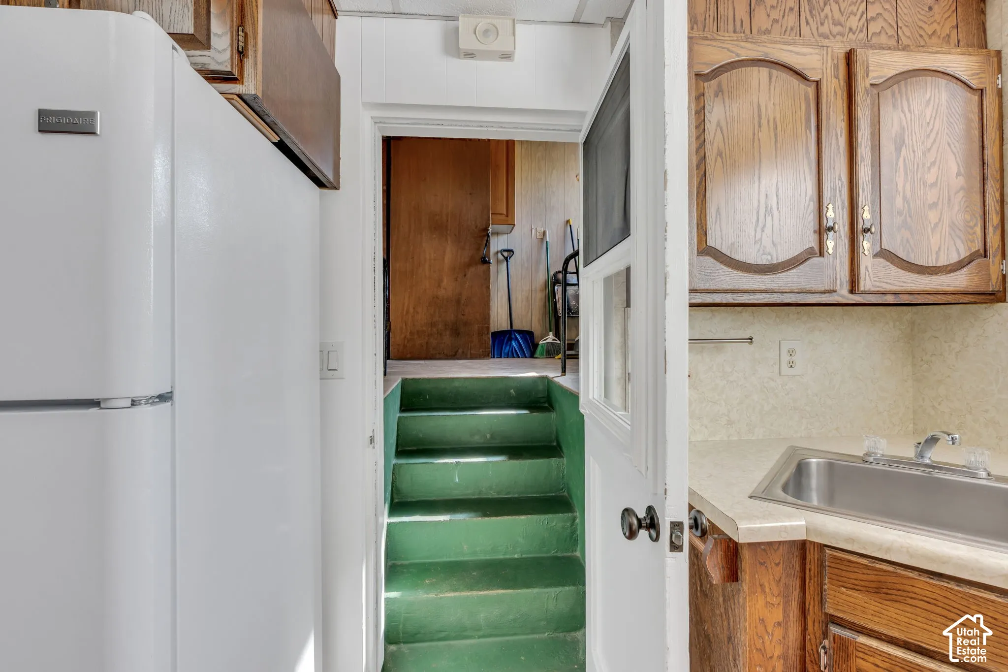 Built-in cabinetry with wood-finish doors, compact stainless steel sink, and white refrigerator