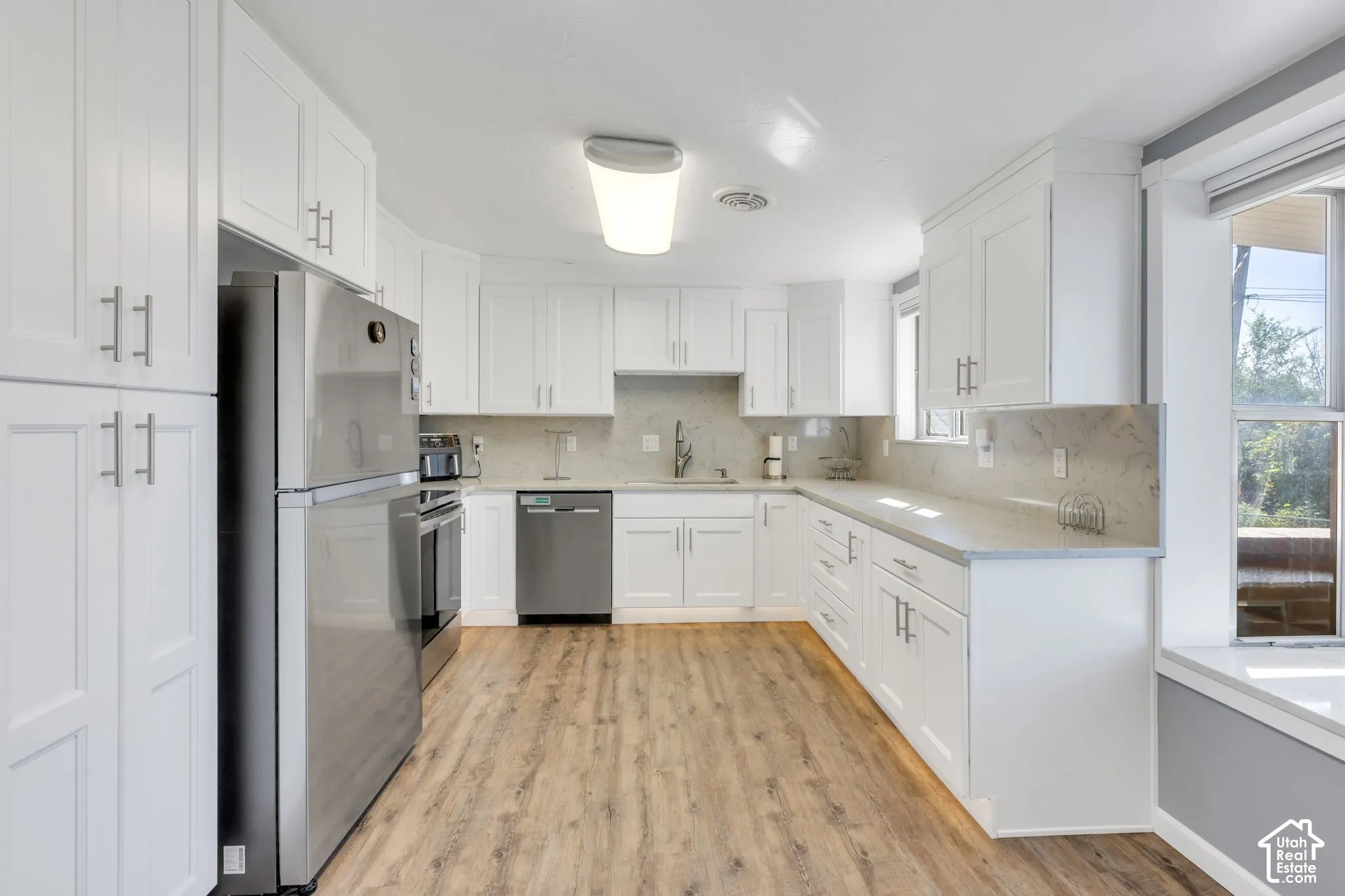 Kitchen featuring wood-finish flooring, white cabinetry with silver hardware, stainless steel appliances, and light-colored countertops with a matching backsplash