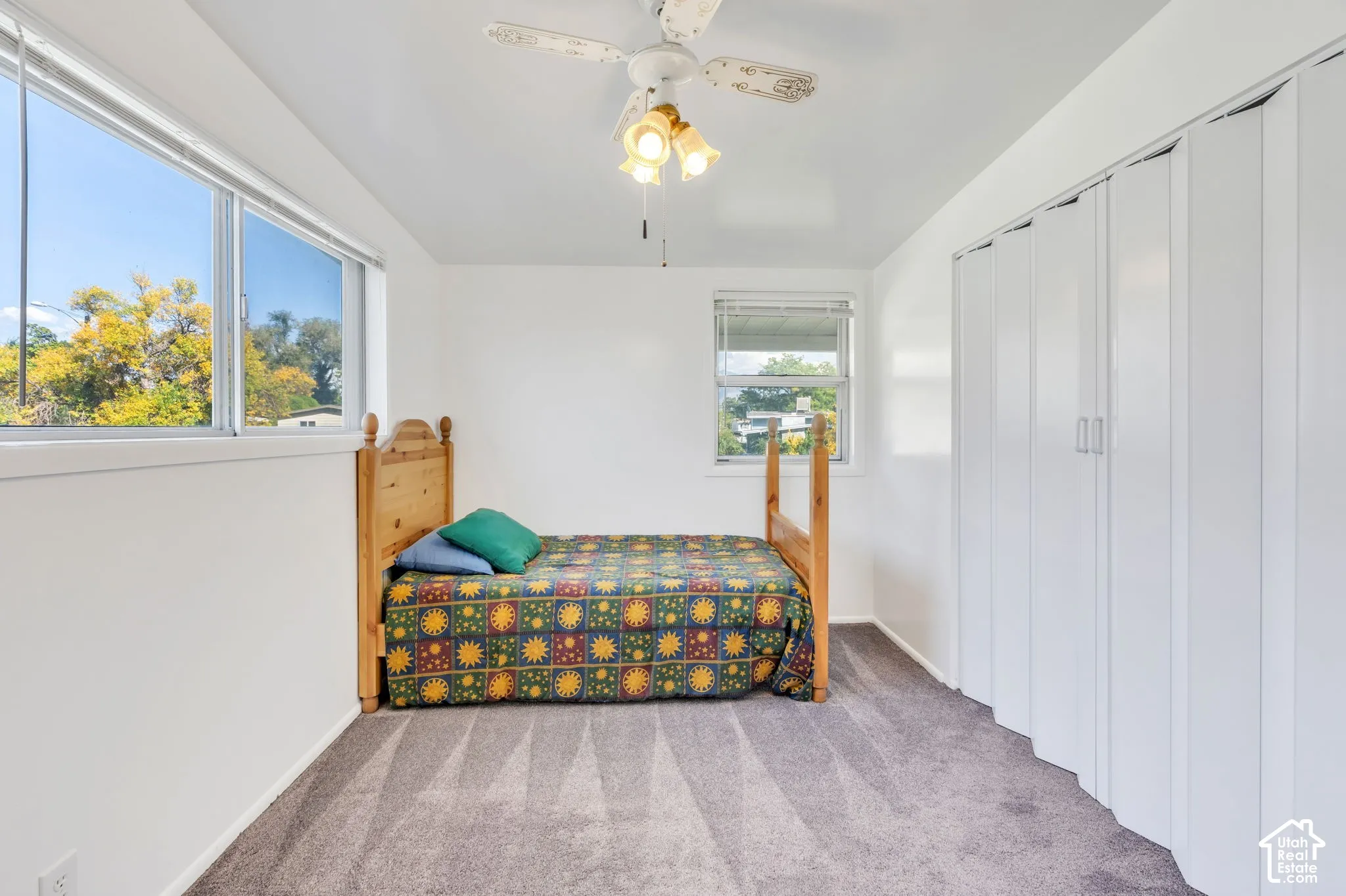 White walls, dual windows, ceiling fan with light fixture, and grey carpet