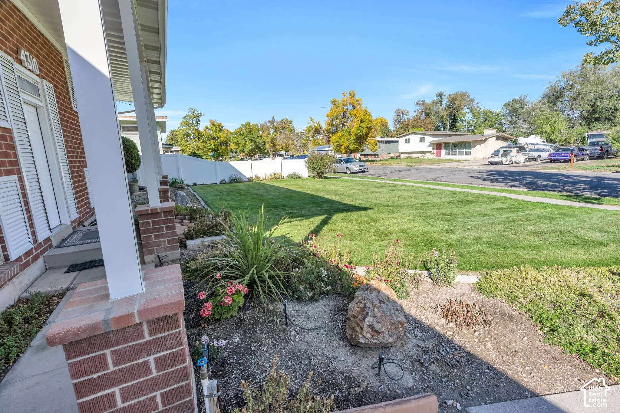 Brick facade with white shutters, expansive front lawn, white privacy fence, and mature landscaping