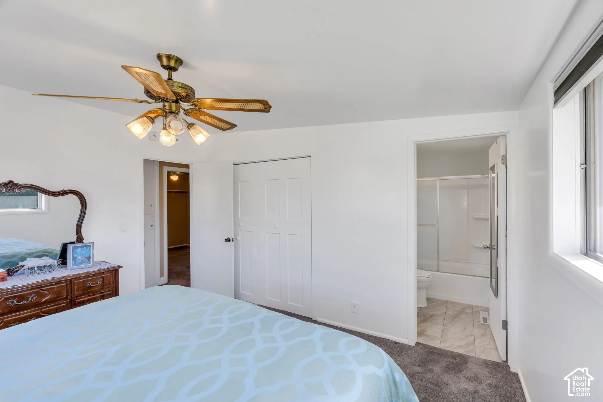 Recessed window with blinds, ceiling fan with integrated lighting, white interior doors, and a bathroom with a white tub and shower surround