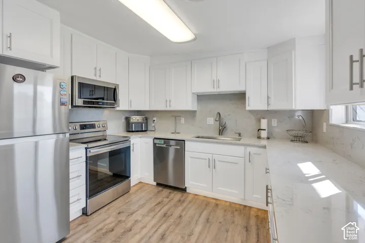 White cabinetry, wood-finish flooring, stainless steel appliances, white countertops, and a full-height backsplash