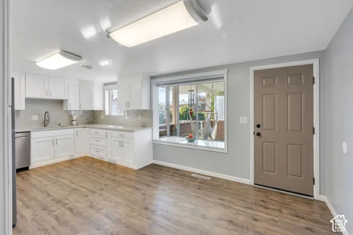 Bright kitchen featuring white cabinetry, light countertops, wood-finish flooring, and a large window