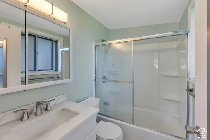 Bathroom featuring a vanity with a white countertop and undermount sink, a tri-fold mirrored medicine cabinet, a light fixture with frosted diffusers, and a shower-over-tub combination with sliding glass doors