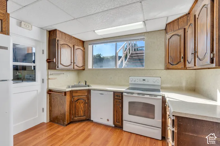 Wood-finish flooring, wood cabinetry, white appliances, and a window above the sink