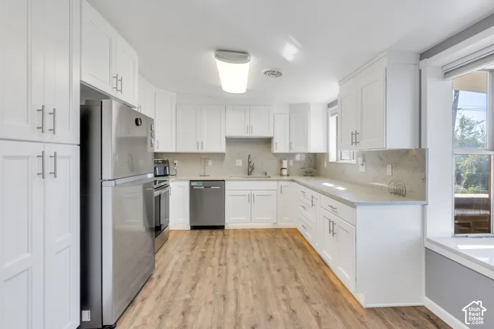Kitchen featuring wood-finish flooring, white cabinetry with silver hardware, stainless steel appliances, and light-colored countertops with a matching backsplash