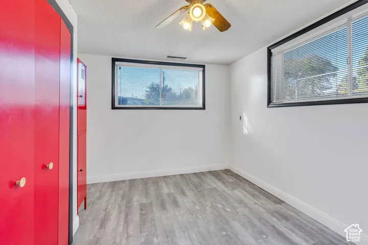Wood-finish flooring, two windows with blinds, ceiling fan with integrated lighting, and red built-in cabinetry