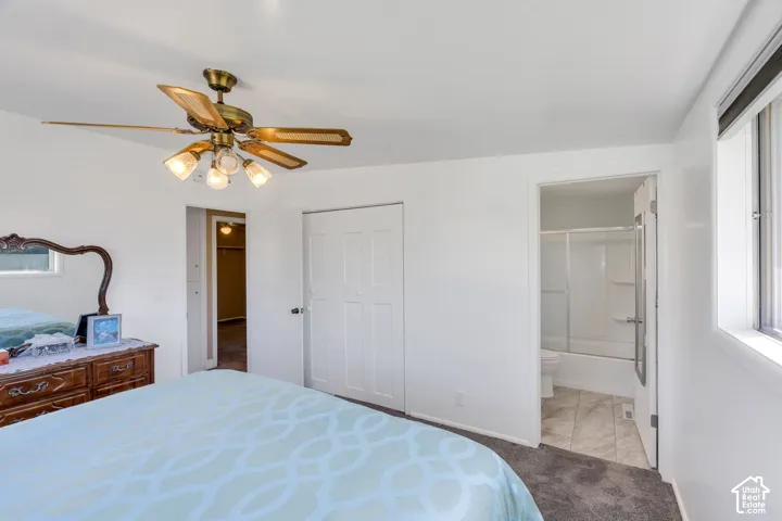 Recessed window with blinds, ceiling fan with integrated lighting, white interior doors, and a bathroom with a white tub and shower surround