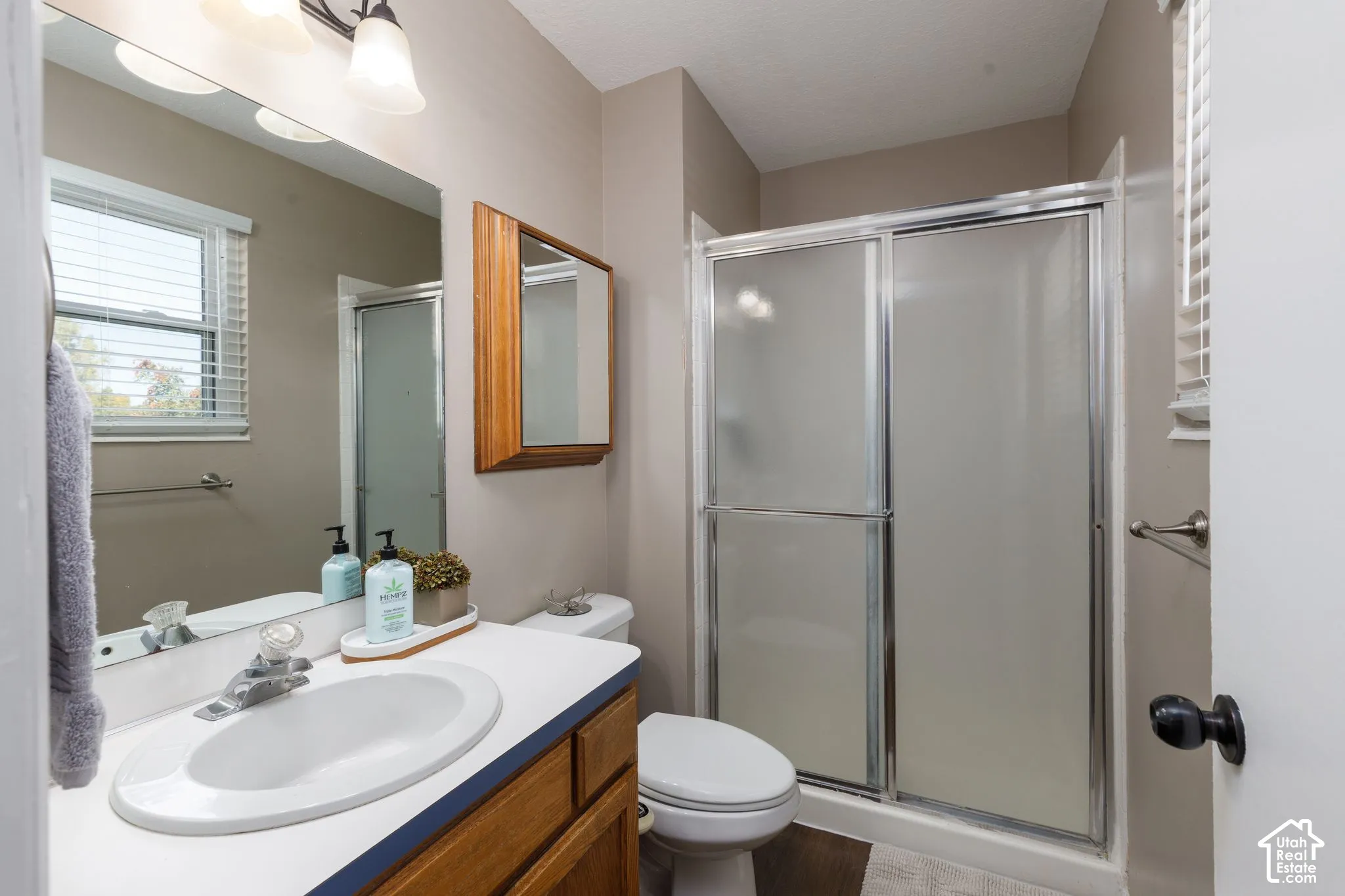 Bathroom featuring a single vanity, wood-finish cabinetry, a toilet, a shower with sliding doors, and a window with blinds