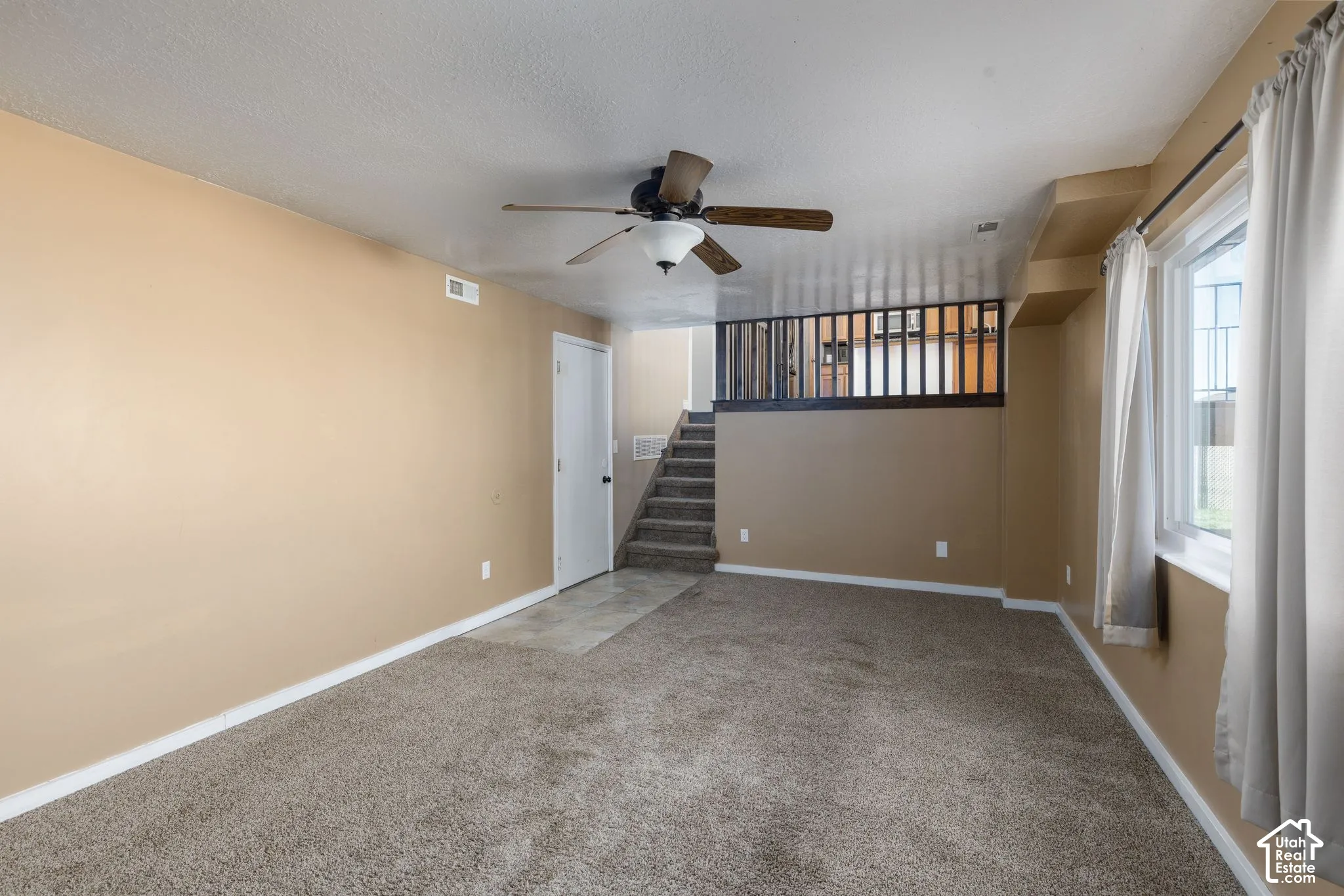 Carpeted flooring, ceiling fan with light fixture, window with white trim, and a staircase with a wood railing