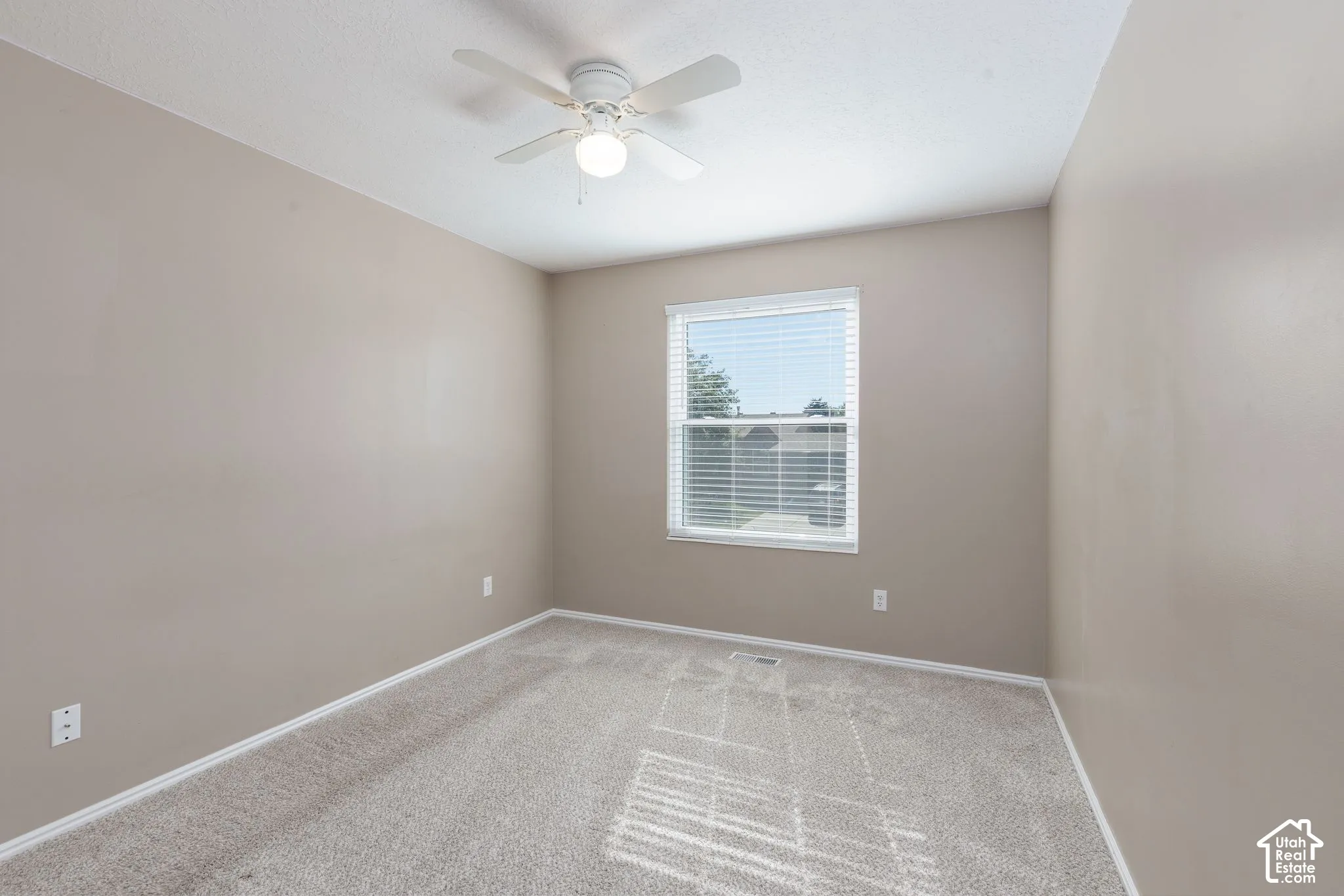 Neutral-toned walls with light-colored carpeting, featuring a window with blinds and a ceiling fan