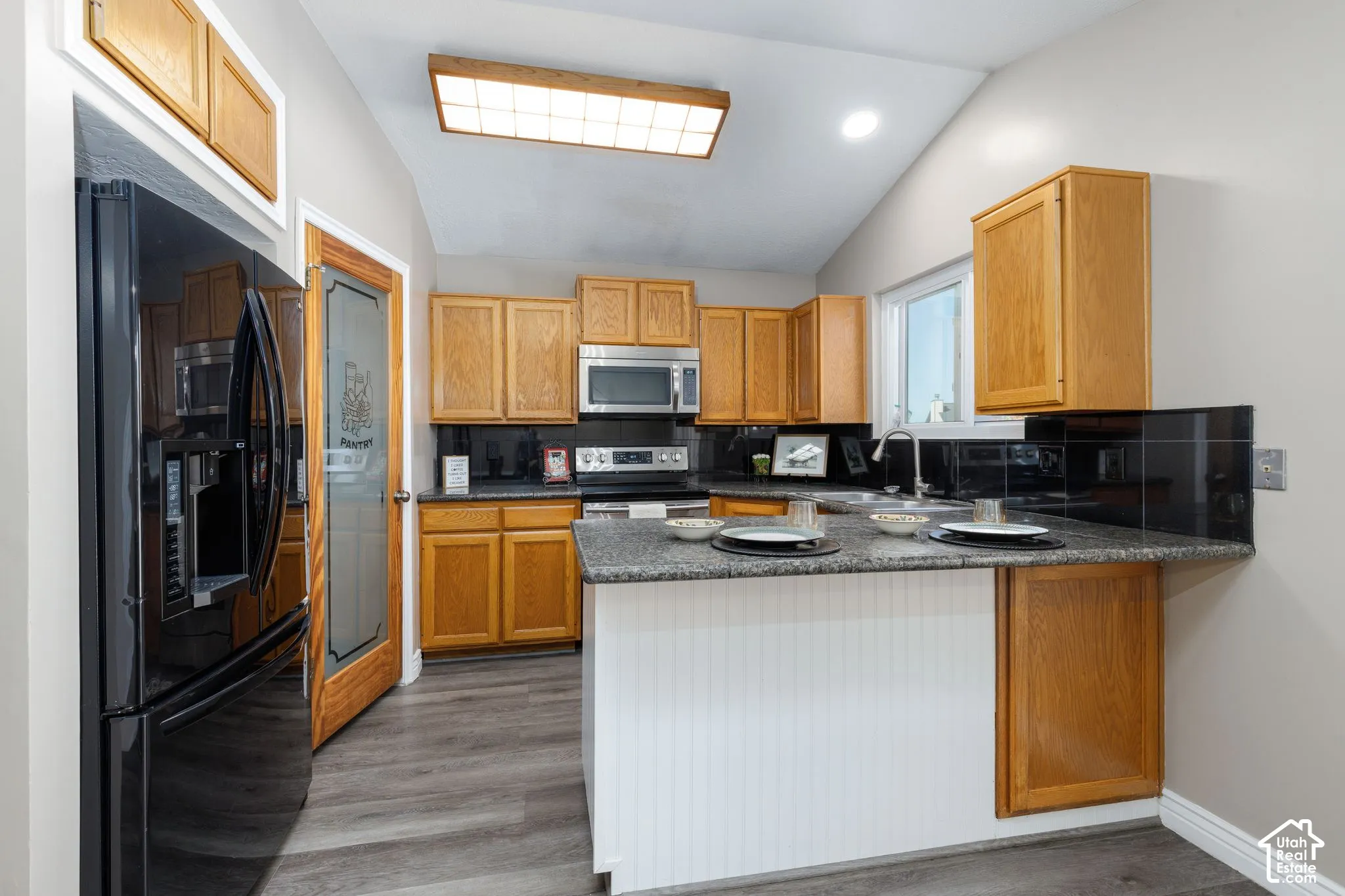 Vaulted ceiling, wood-finish flooring, wood cabinetry, stone countertops, and a built-in kitchen island with white paneling