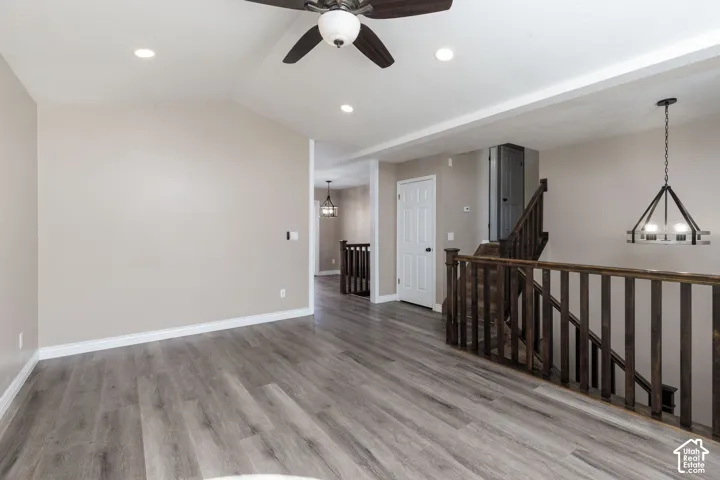 Vaulted ceiling, wood-finish flooring, recessed lighting, ceiling fan, and dark wood baluster railing