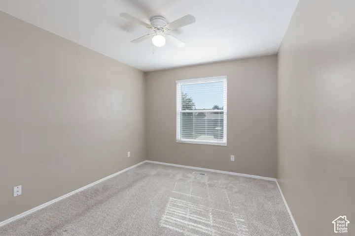 Neutral-toned walls with light-colored carpeting, featuring a window with blinds and a ceiling fan