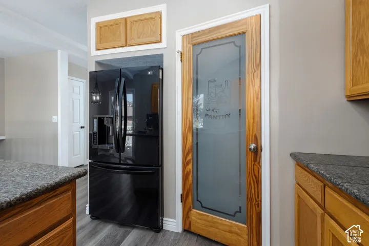 Built-in black refrigerator, wood-finish pantry door with frosted glass, wood-finish cabinetry, and speckled countertops