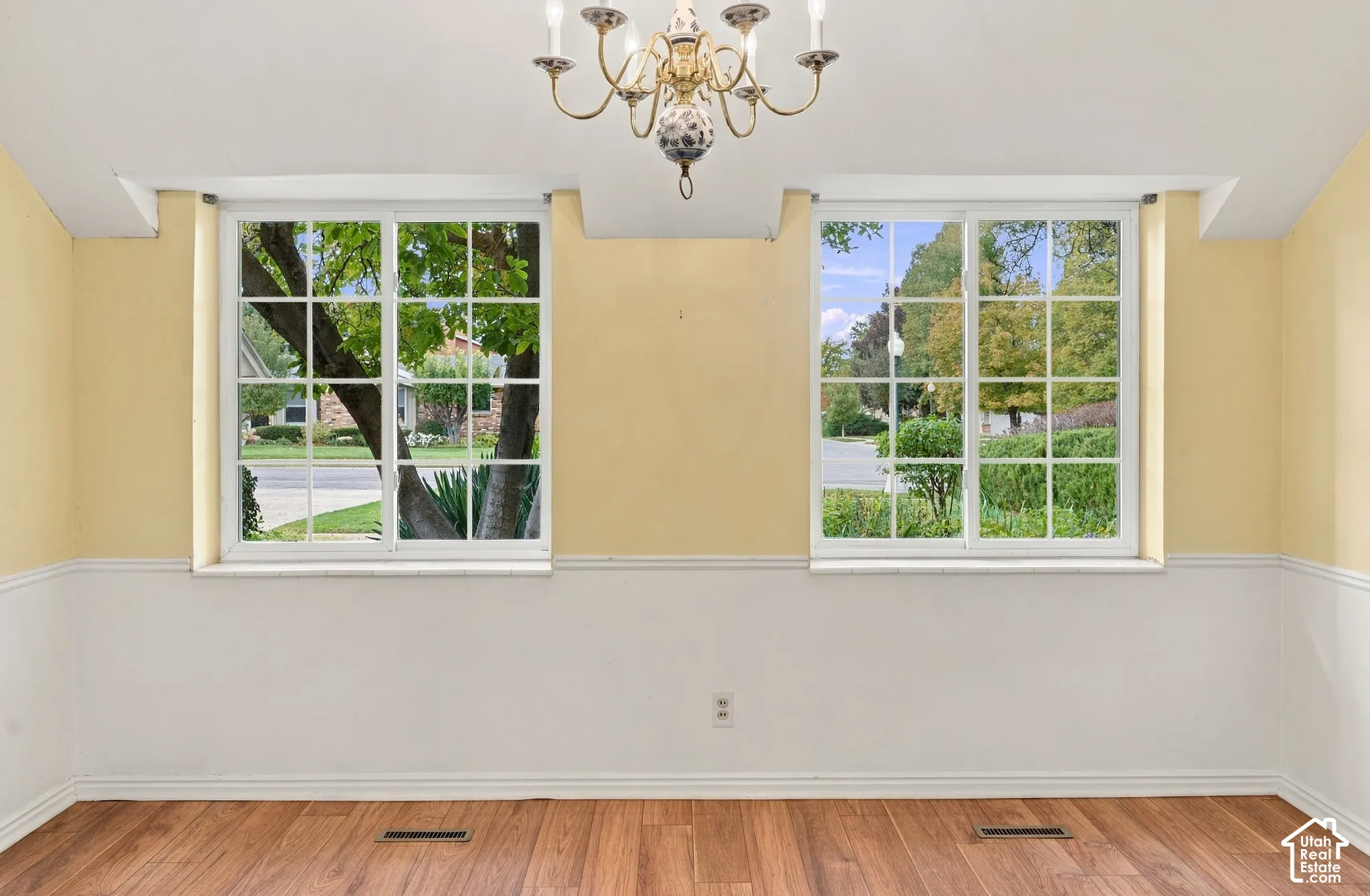Wood-finish flooring, dual grid-pattern windows, decorative chair rail molding, and a multi-arm chandelier