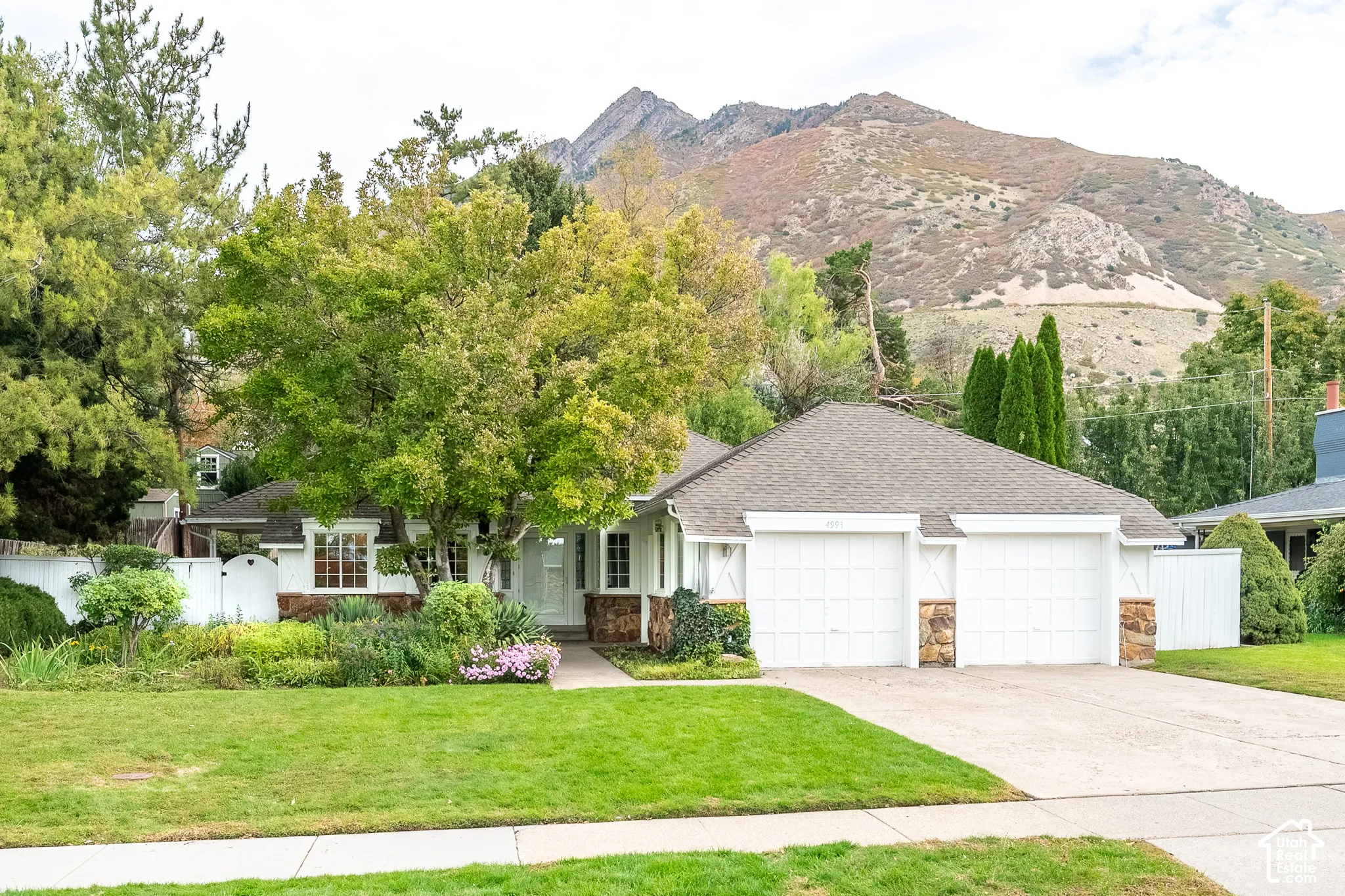 Holladay residence featuring stone masonry accents, an attached two-car garage, established landscaping, and mountain backdrop