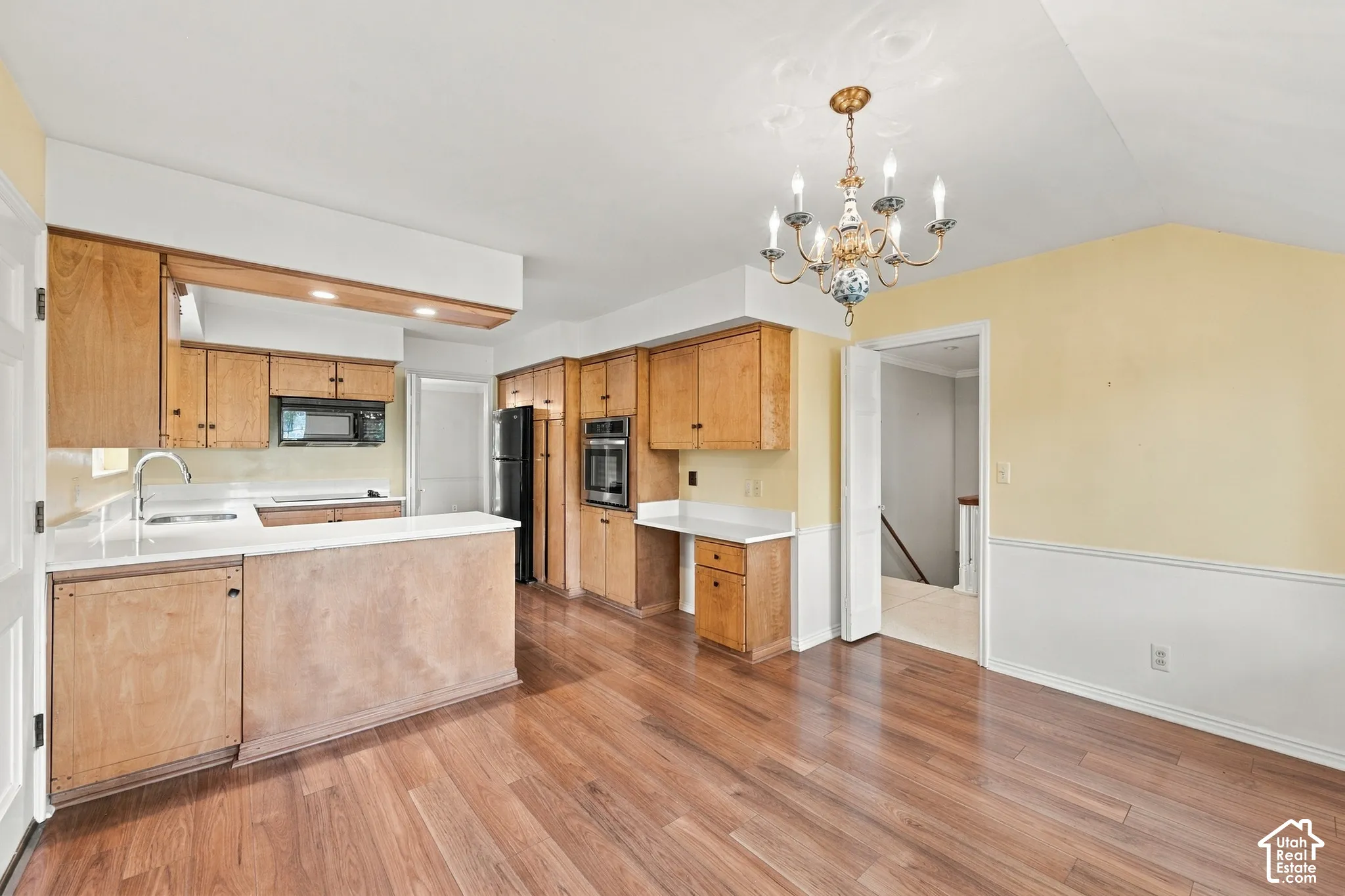Kitchen featuring wood cabinetry, integrated oven, built-in desk, wood-finish flooring, and a multi-arm chandelier